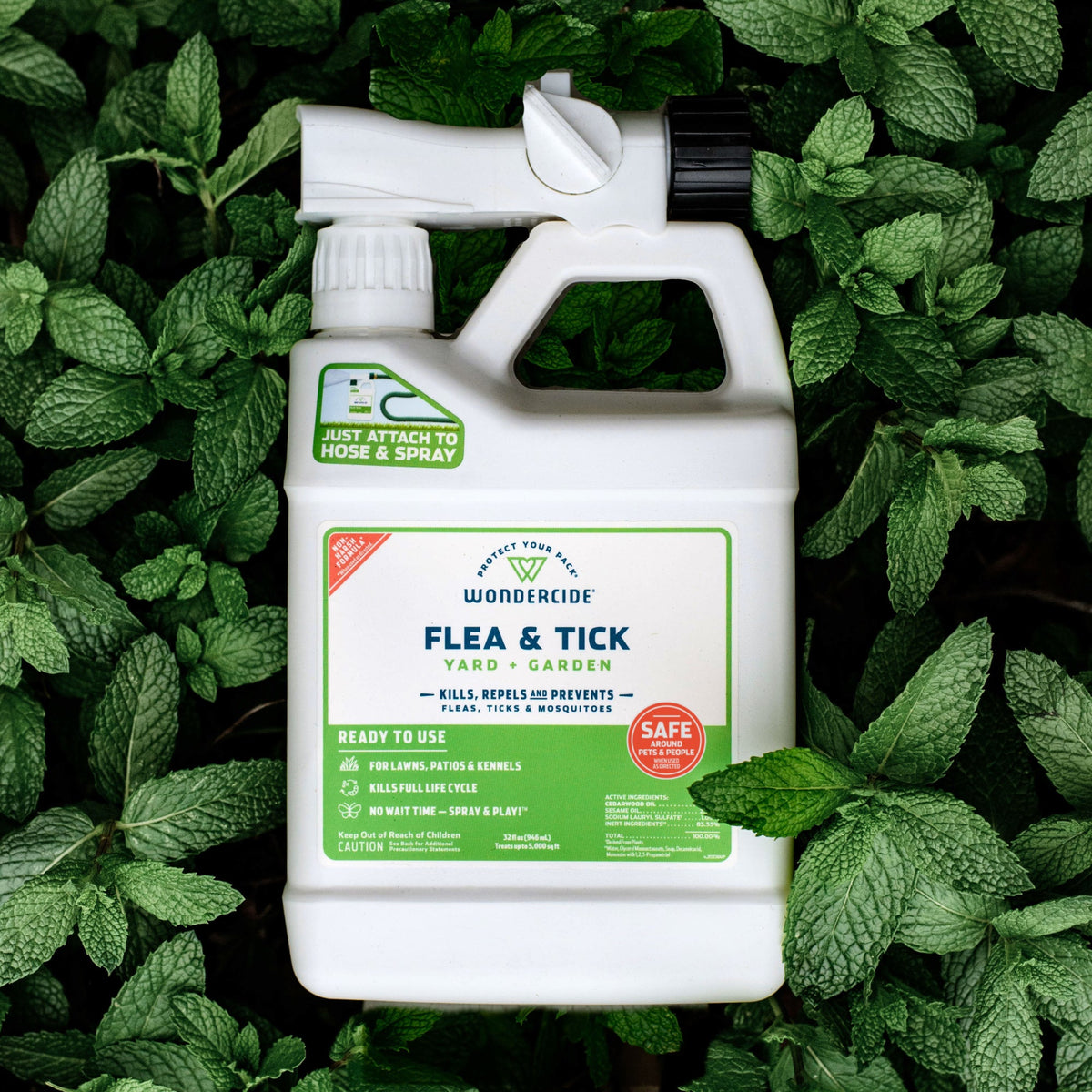 A white bottle of Wondercide Ready-to-Use Flea & Tick Spray for Yard + Garden sits on green mint leaves, featuring a hose attachment and green label that highlights its pet- and family-safe formula for flea and tick protection.