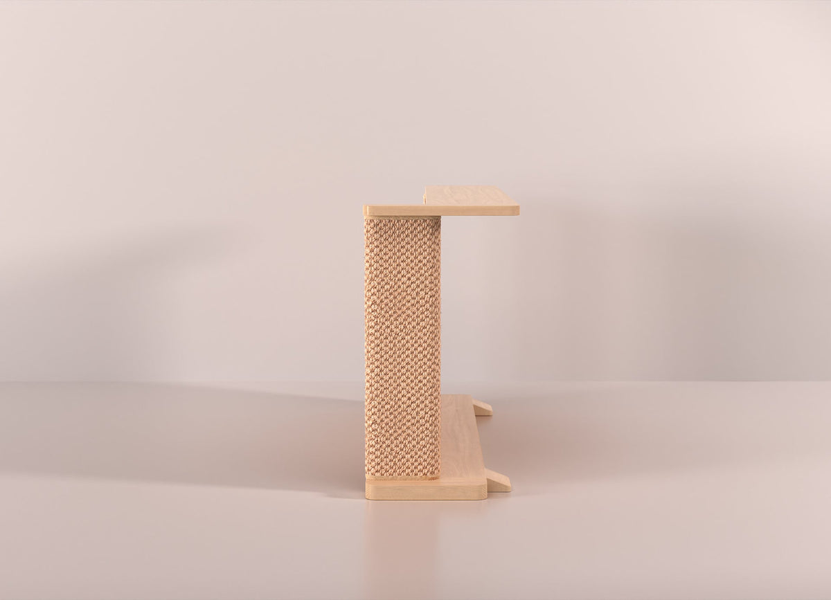 A Cat-e-Corner table placed next to a sofa, integrating a cat's scratching post with a small table, in a room with a plant and a colorful cushion.