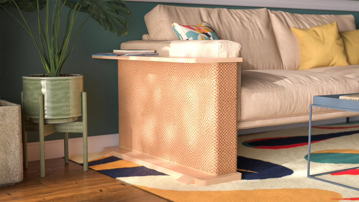 A Cat-e-Corner table placed next to a sofa, integrating a cat's scratching post with a small table, in a room with a plant and a colorful cushion.