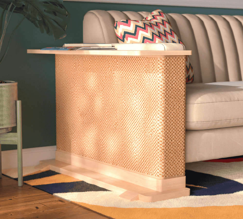 A Cat-e-Corner table placed next to a sofa, integrating a cat's scratching post with a small table, in a room with a plant and a colorful cushion.